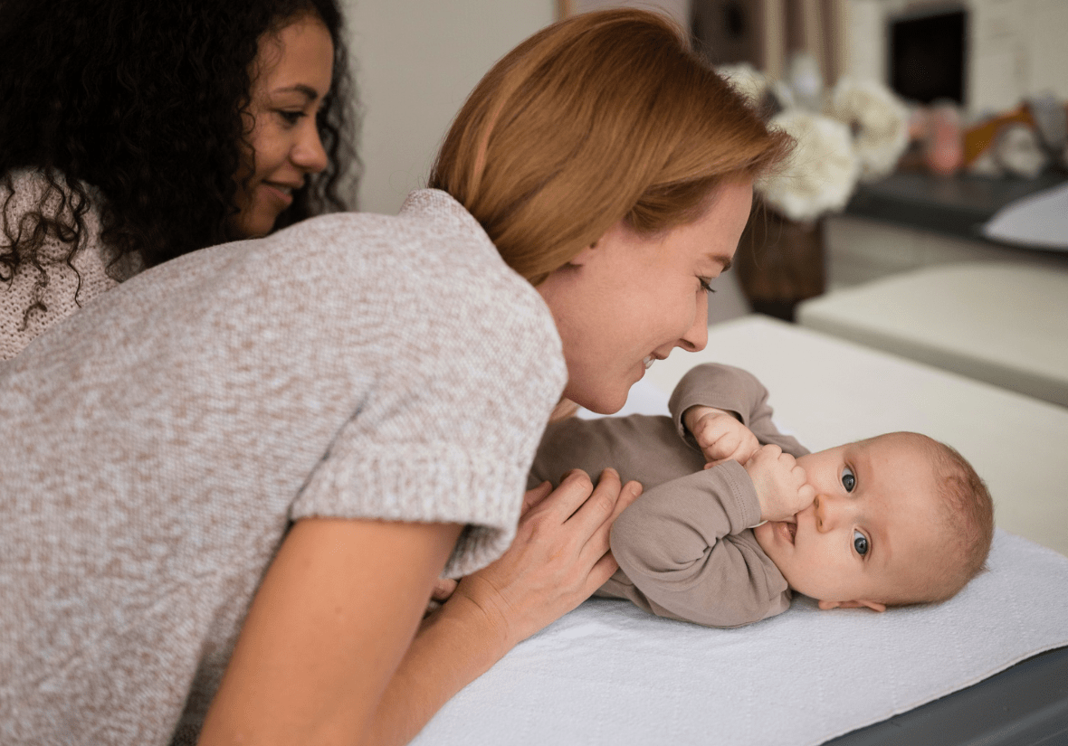 Two woman's attending to a baby on a changing table.