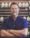 A man stands before shelves filled with various pill bottles