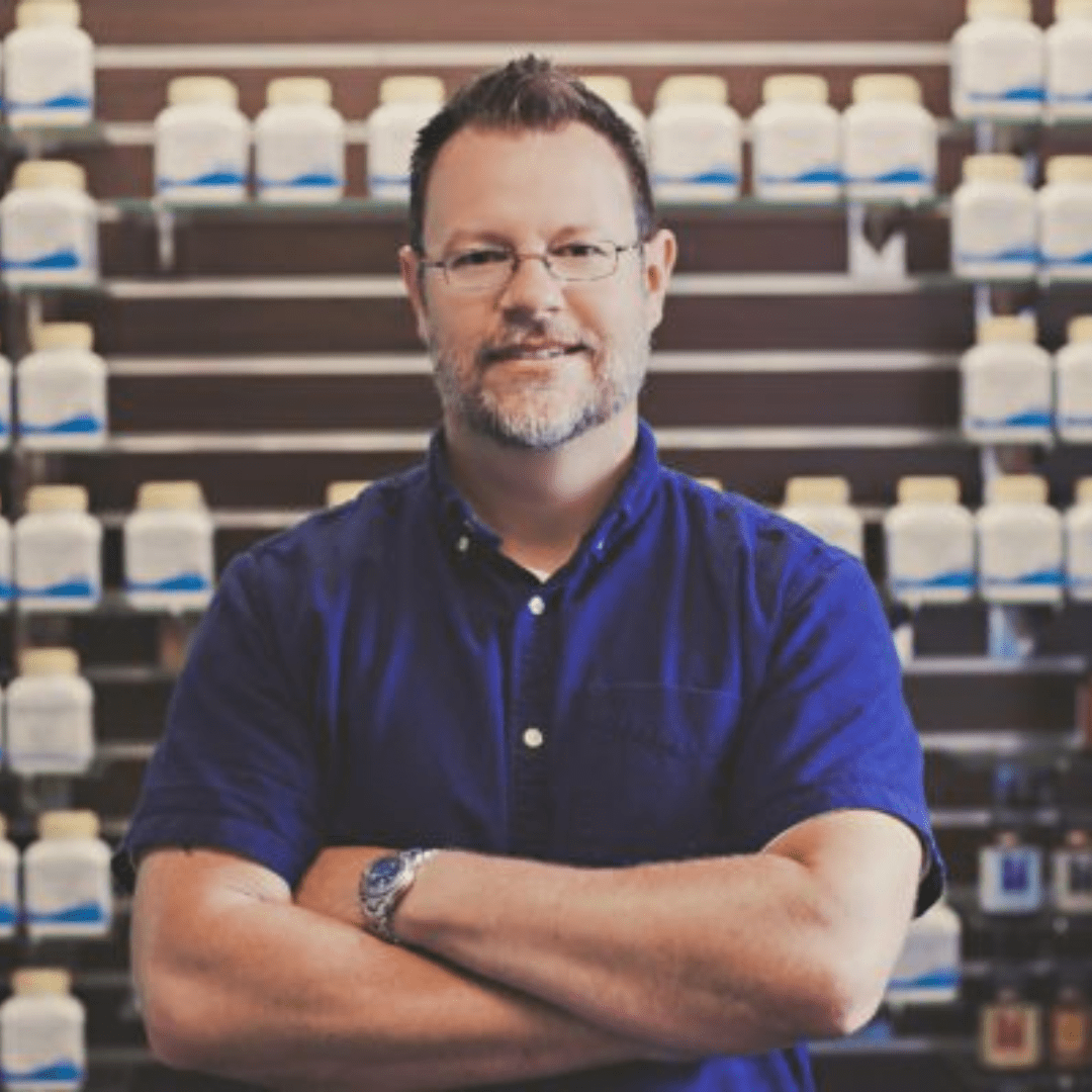 A man stands before shelves filled with various pill bottles