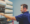 A person in a blue shirt restocking shelves with bottles