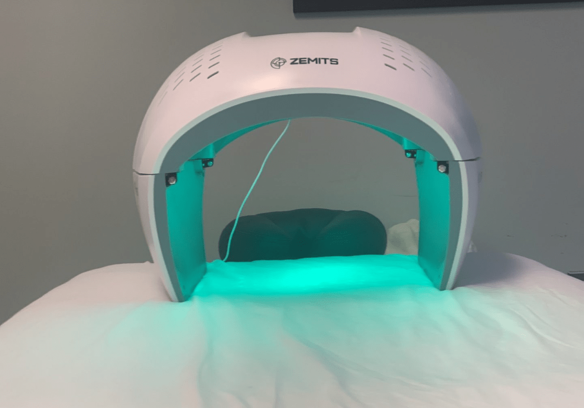 A Zemits branded LED light therapy dome emitting a teal glow over a treatment bed.