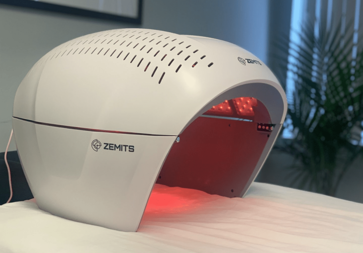 A Zemits LED light therapy device for skin treatment, switched on with red light, on a table.