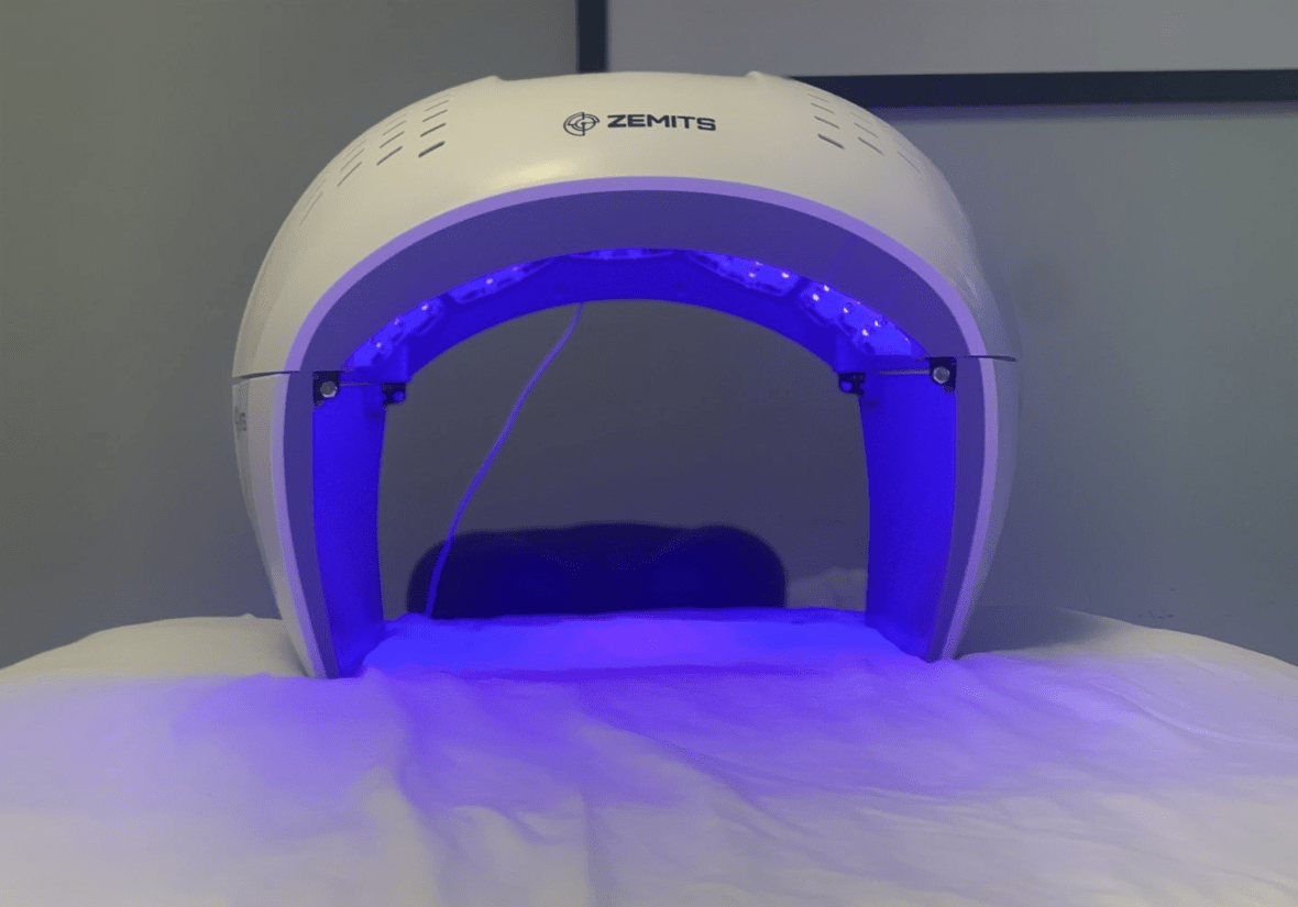 A Zemits skincare device emitting blue light over a treatment bed.